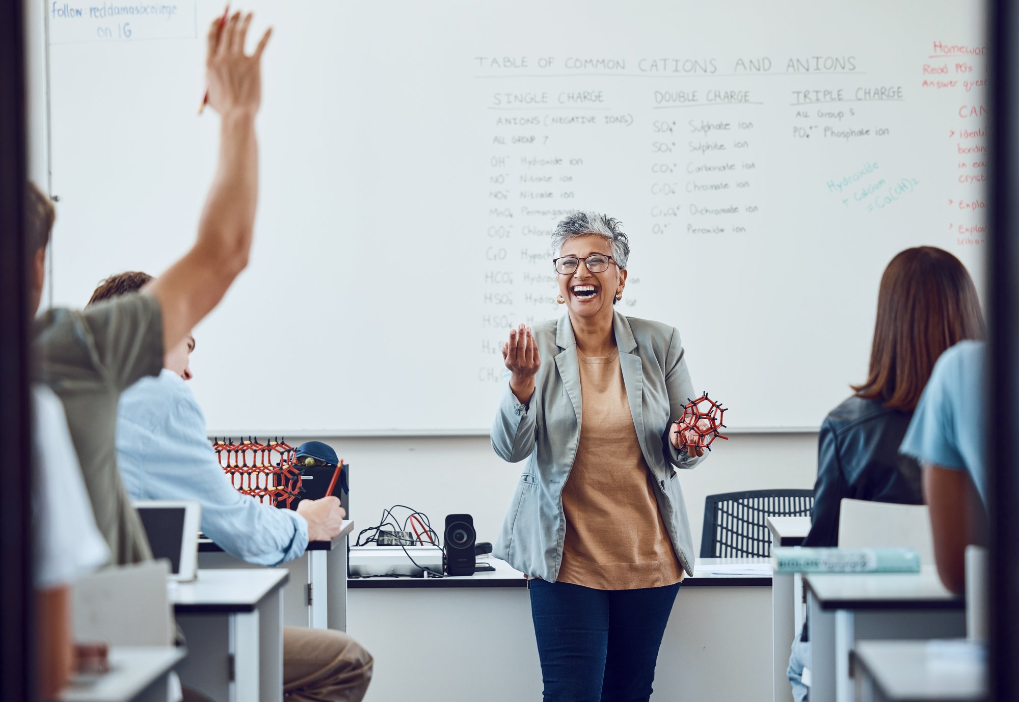 A female professor with short gray hair smiling and delivering a lecture in front of a classroom of college students