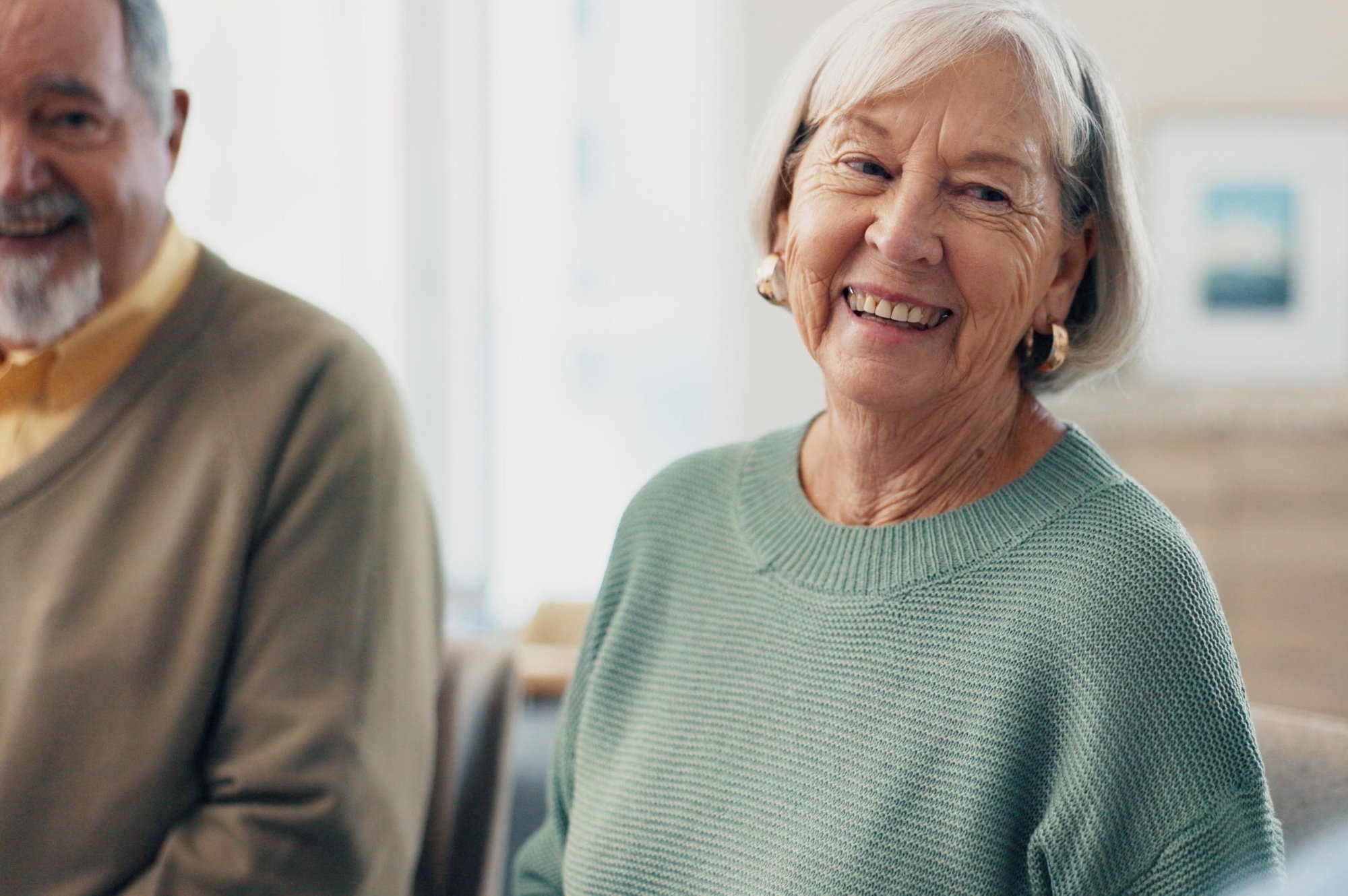 A smiling elderly woman with short grey hair wearing a green sweater