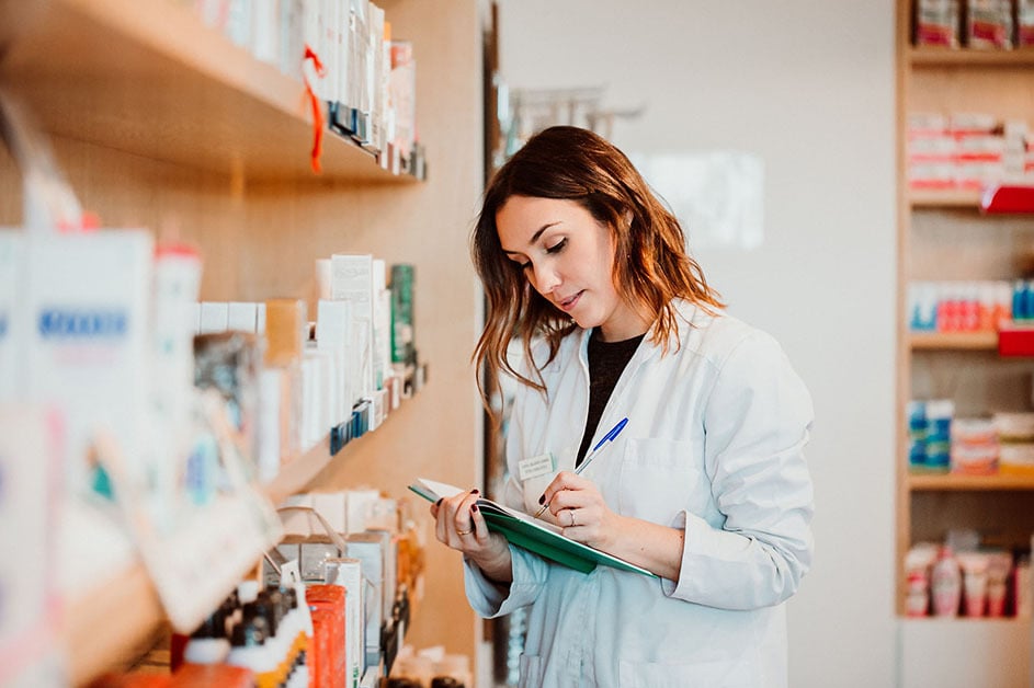 Young female pharmacist working in her large pharmacy taking inventory