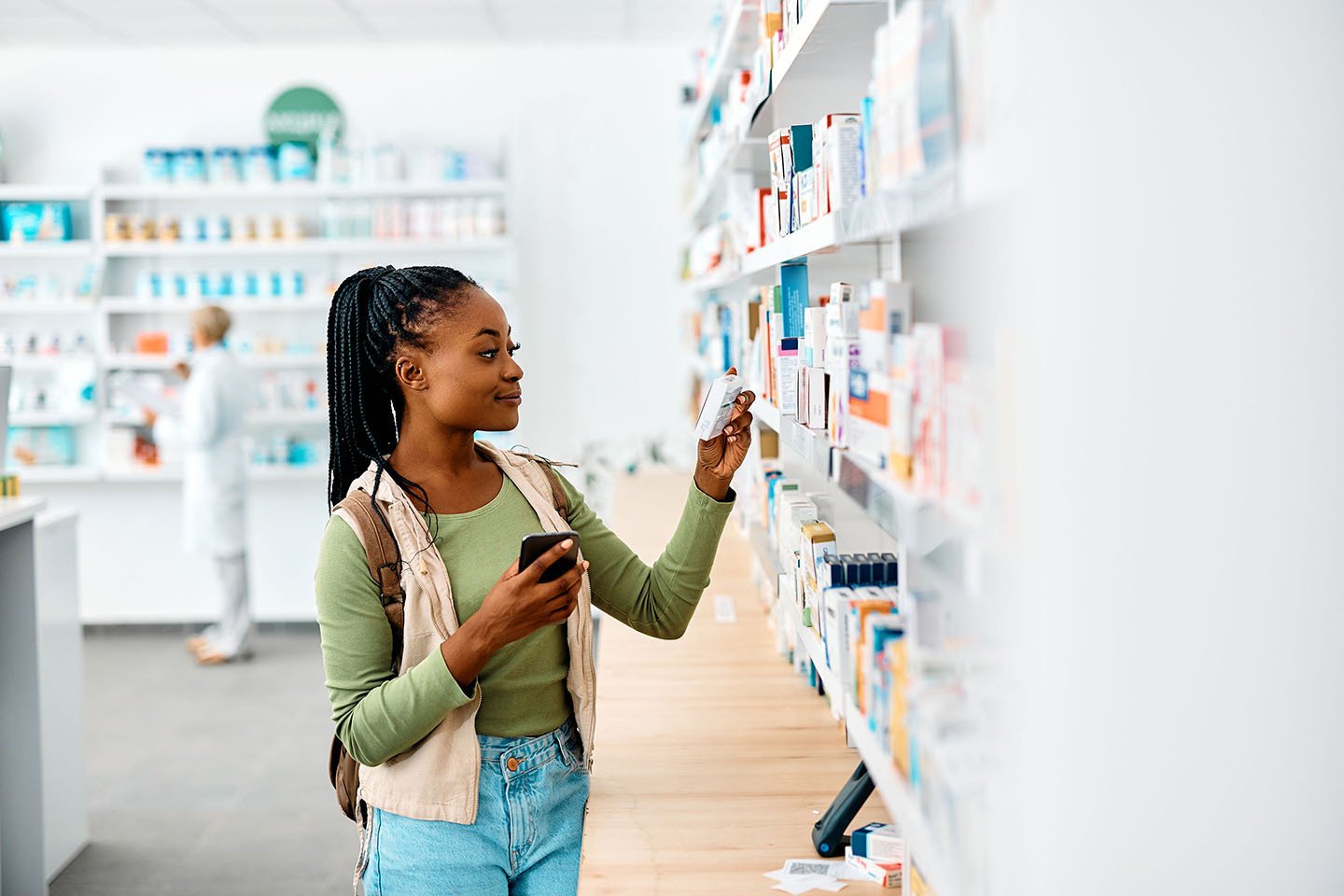 Young black woman using cell phone while looking for medicine in pharmacy