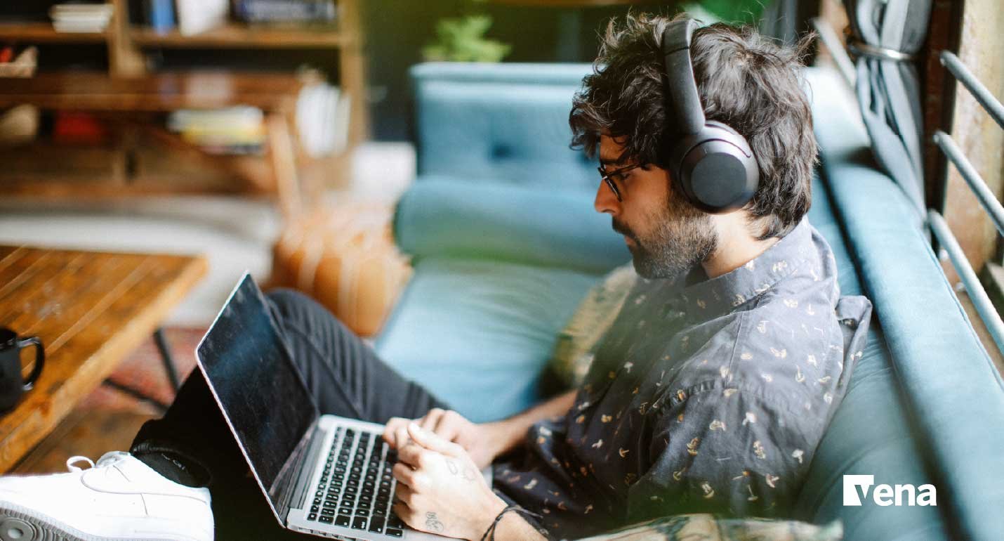 A man wearing headphones and sitting on a couch with a laptop in front of him