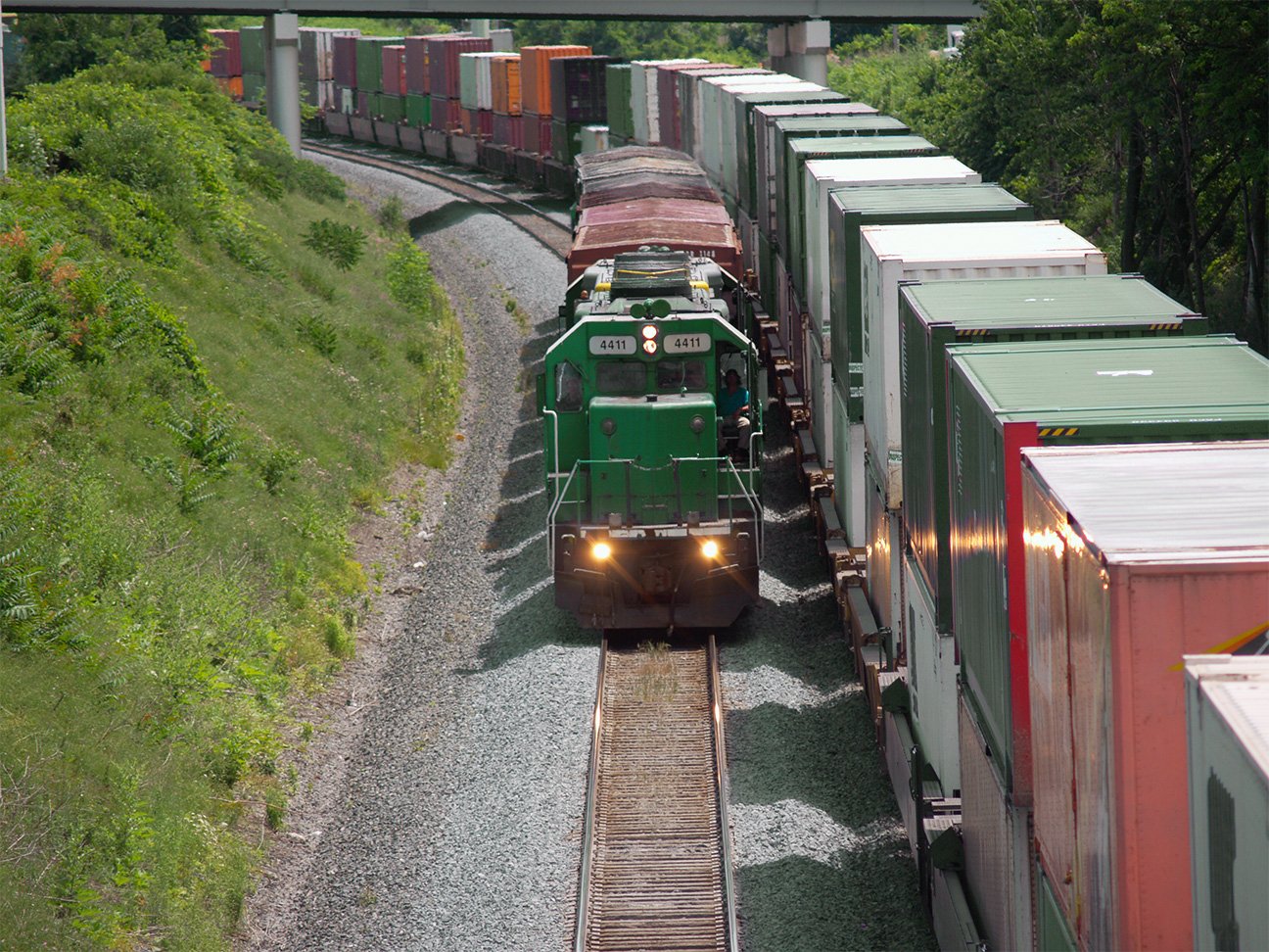 Locomotive pulling short train beside parked container cars