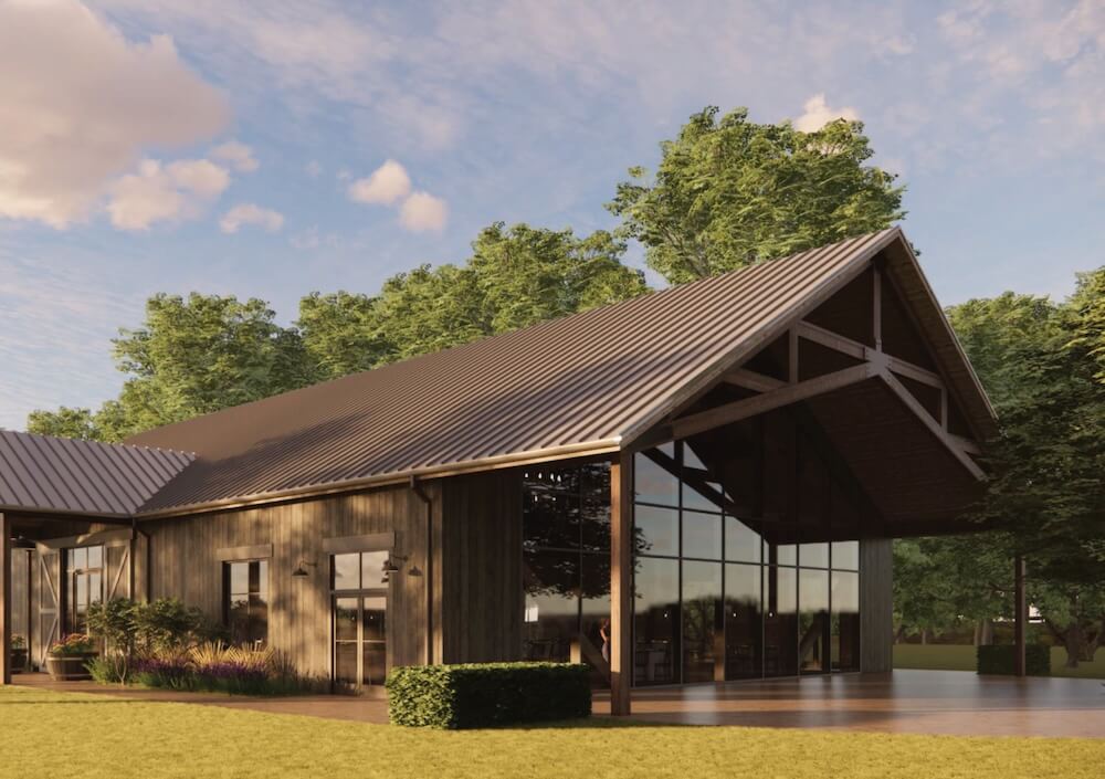 Modern barn-style building with metal gabled roof, wood siding, and large glass wall, set among trees on a sunny day.