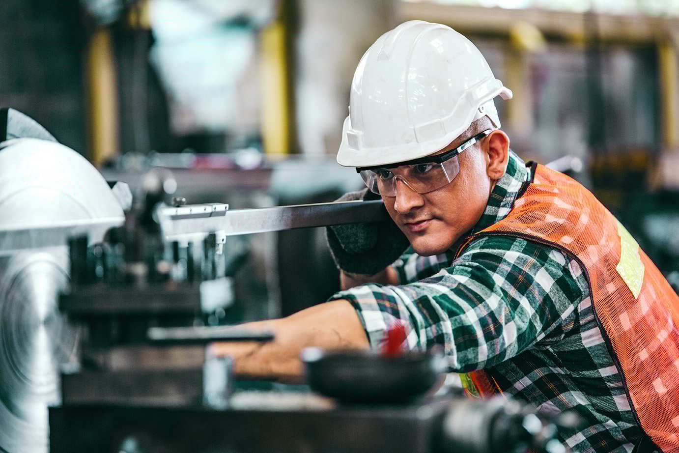 Male engineer metalworker industrial experienced operator technician worker in safety hard helmet working on lathe machine