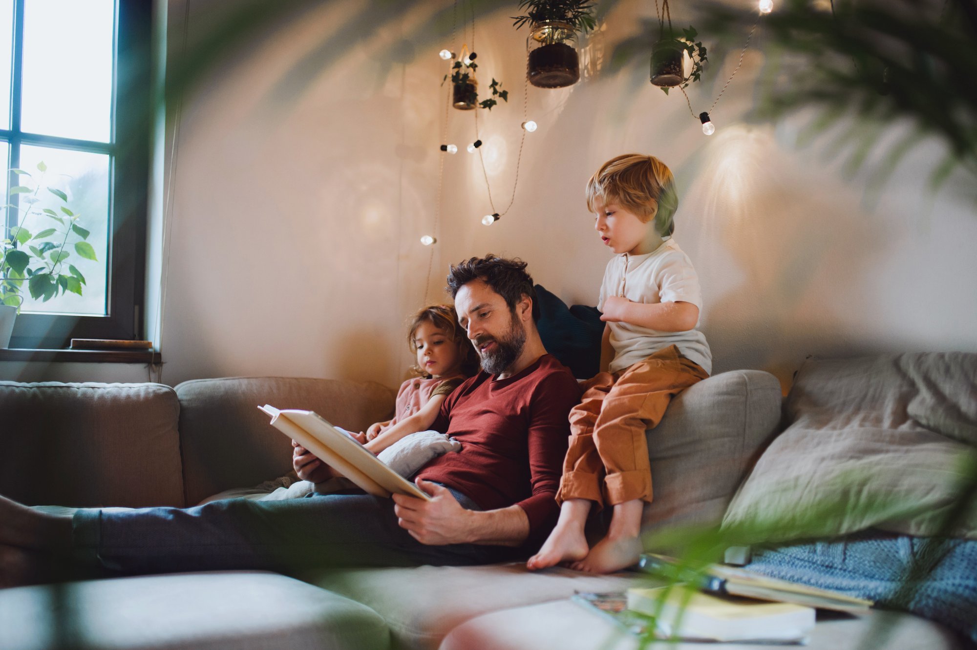 Mature father with two small children resting indoors at home, looking at photo album