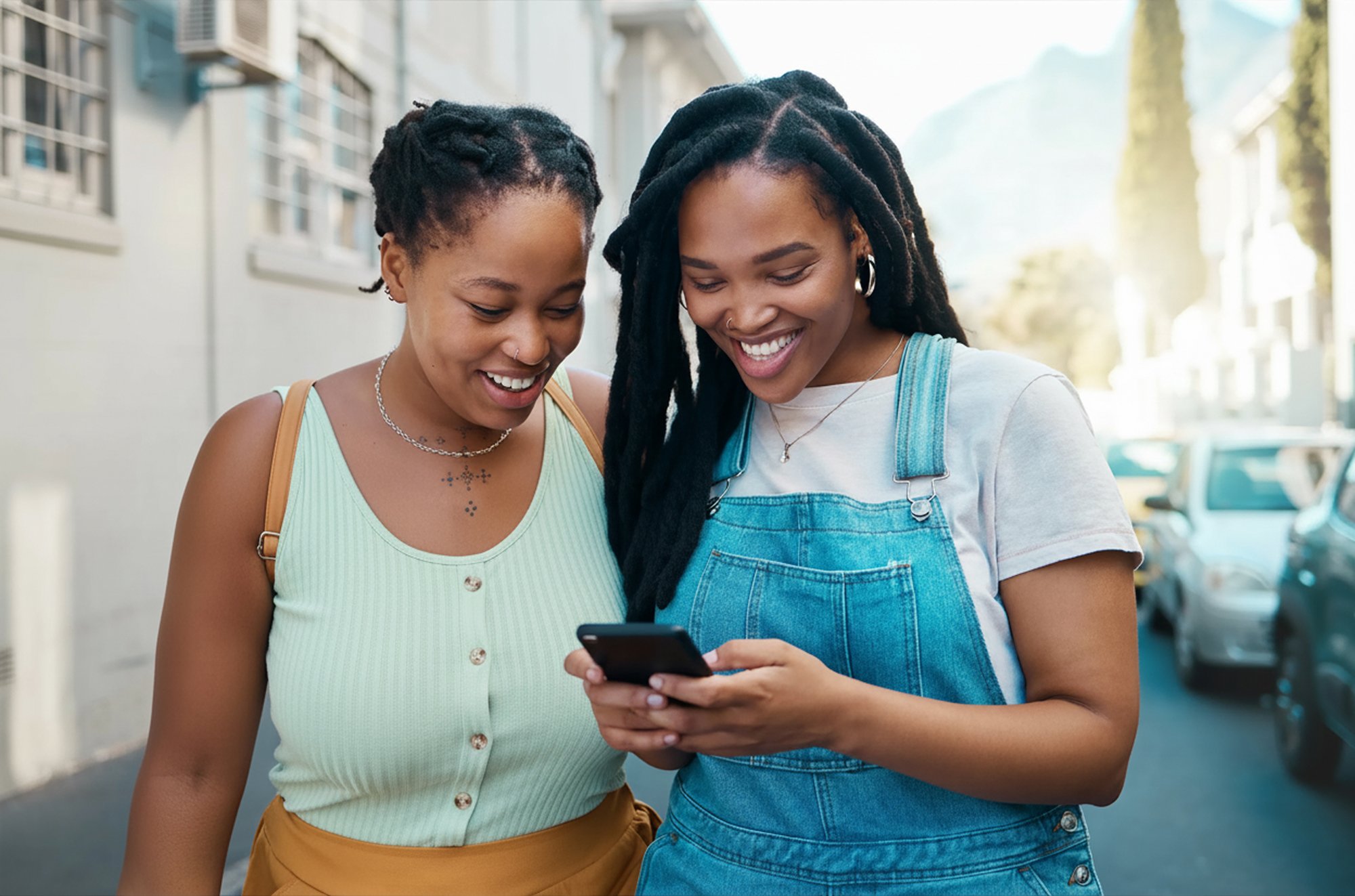 Happy black female friends on a phone, texting together outside on the street