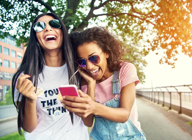 Image of two woman outside walking, laughing and listening to music