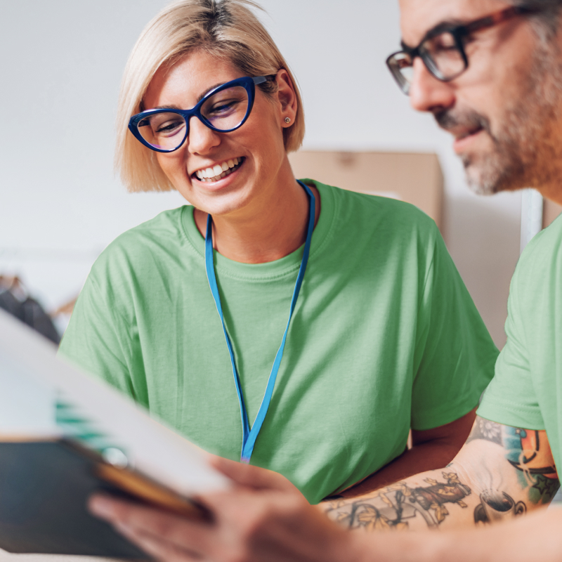 Two nonprofit team members with green t-shirts and blue lanyards around their necks excitedly reviewing planning materials together