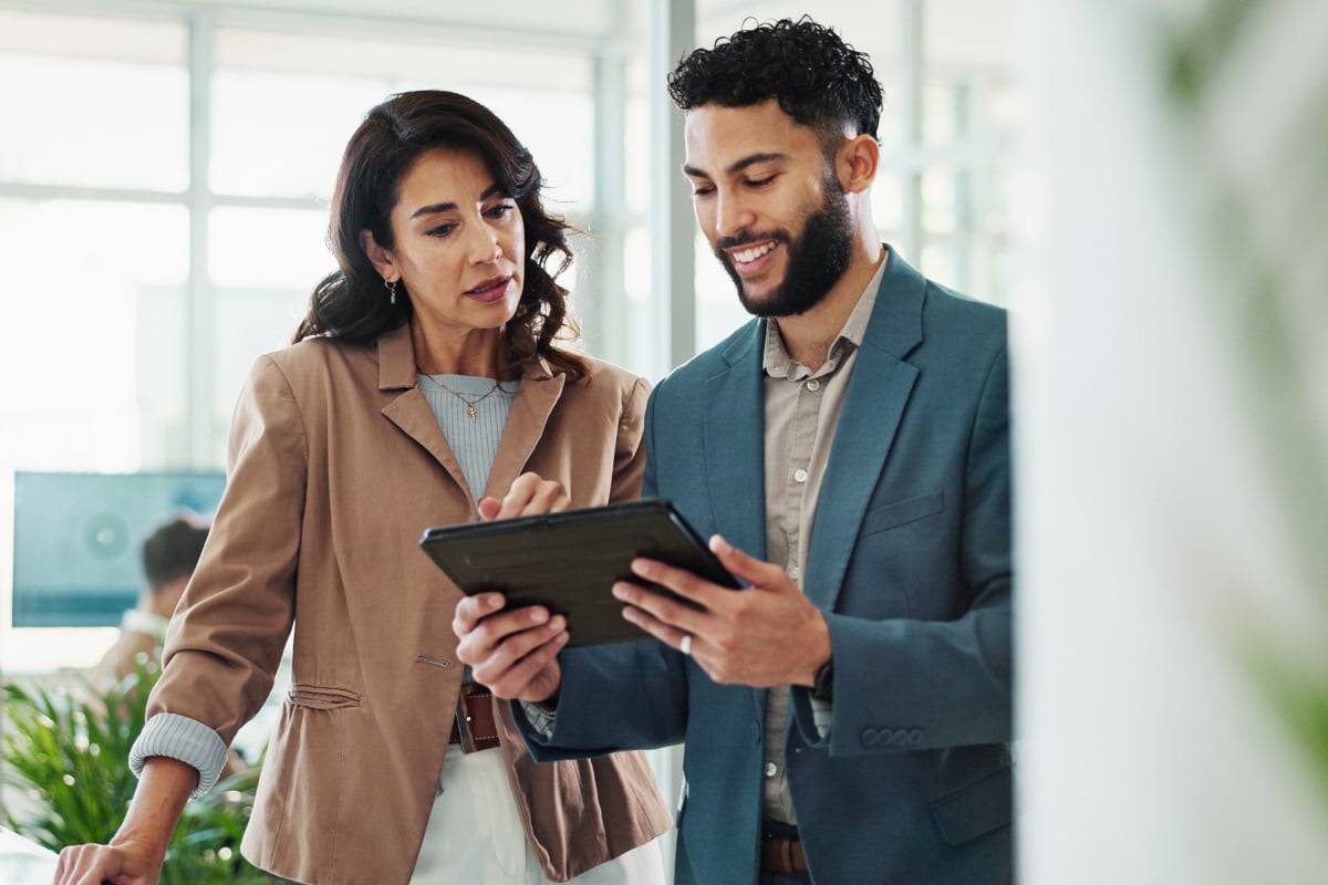 A man and woman in business attire are collaborating while looking at a tablet together.