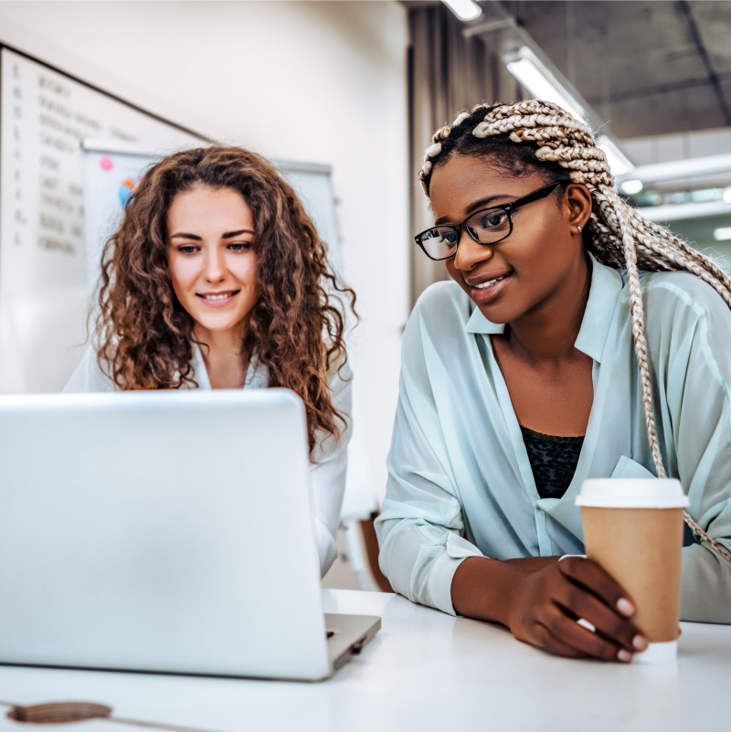 A White woman and a Black woman looking at a laptop screen together
