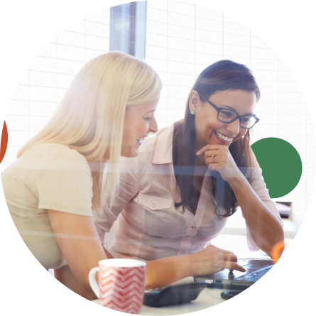 Two women sitting at a desk, smiling and looking at a laptop screen