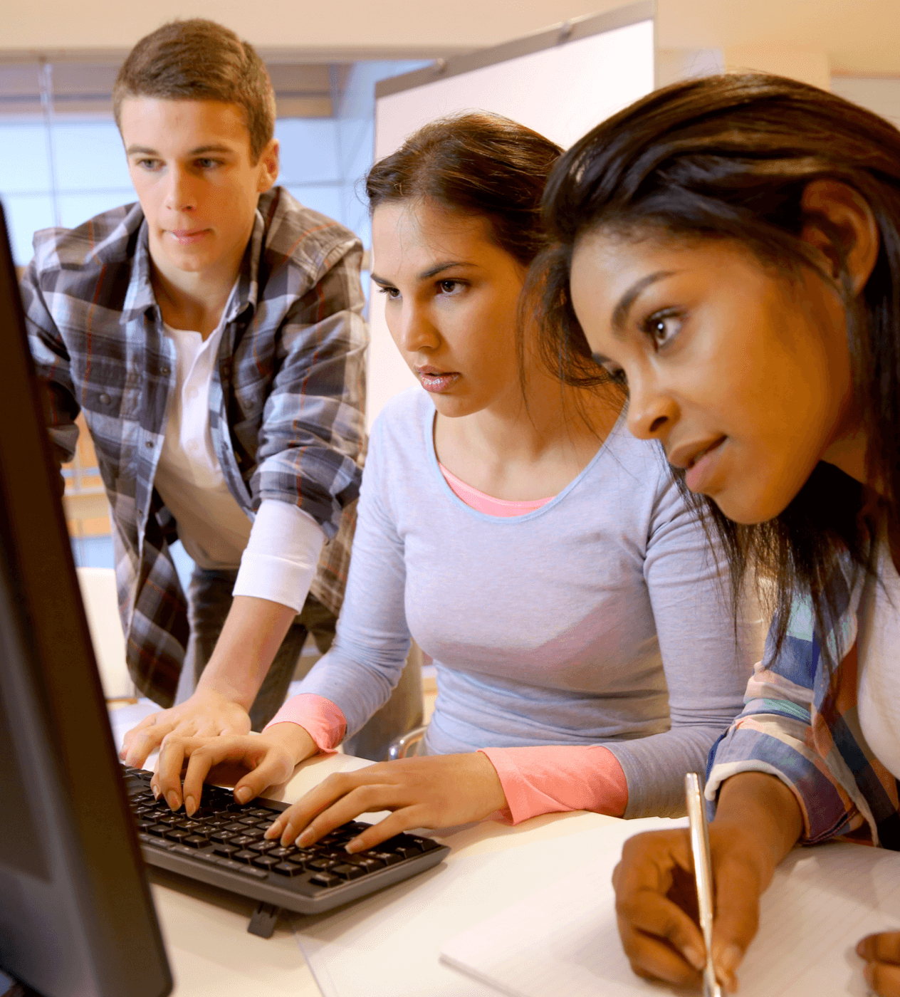 Group of students working diligently at a computer screen.